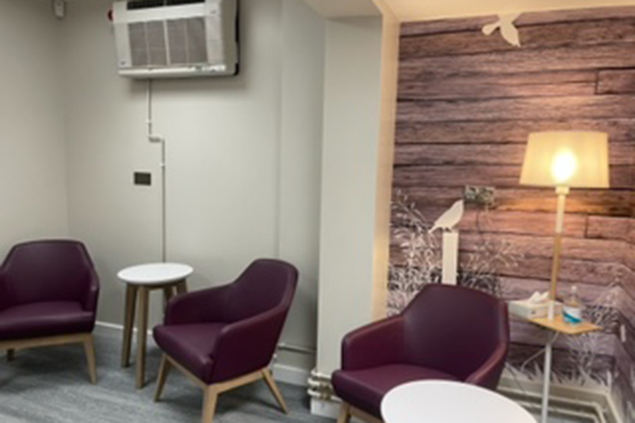 A room with purple armchairs and a lit corner standard lamp.  The wall features a mural with light purple wood effect and bird silhouettes.