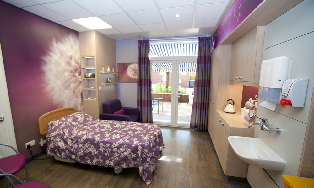 A bedroom with cupboards and sink, decorated in co-ordinating purple colours.  The mural above the bed shows a dandelion head.