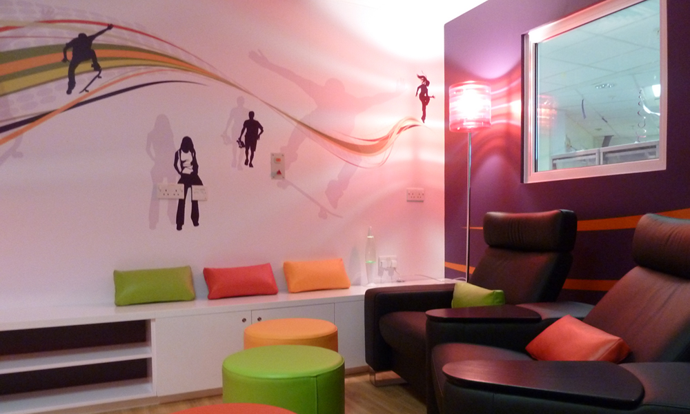 A room with colourful furniture including plush chairs and stools and wall art depicting various sports.