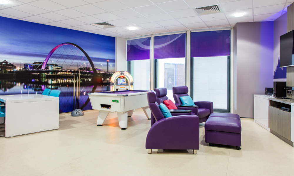 Teenage Cancer Trust hospital room containing pool table with purple cloth, purple chairs, wall art depicting London scene with purple colours and table with co-ordinating turquoise chairs.
